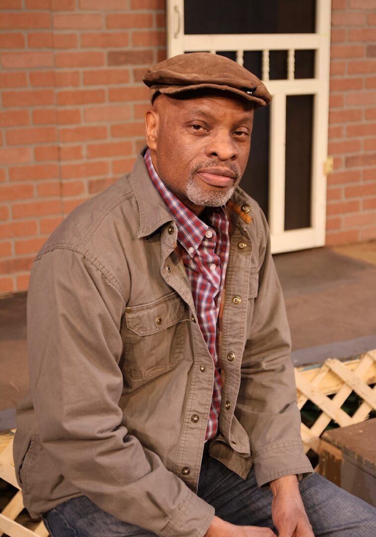 A man in brown jacket and hat sitting on bench.